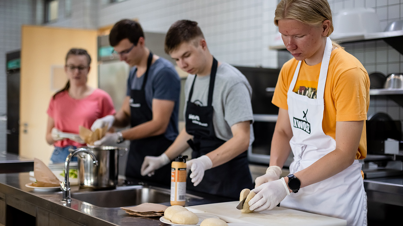 Vier Jugendliche stehen in einer Küche und kochen.