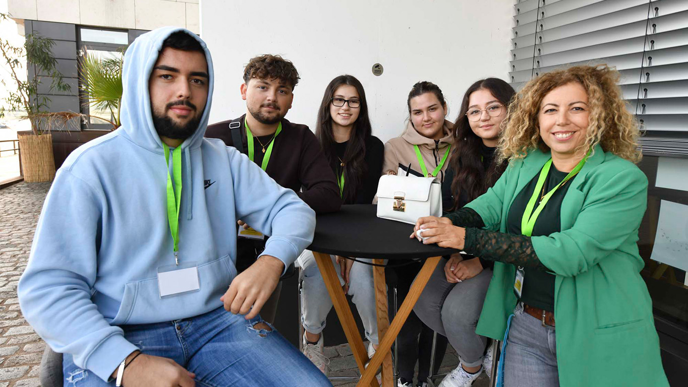 Fünf Schüler und Schülerinnen einer Schülerfirma sitzen mit ihrer Lehrerin an einem Tisch vor dem Gebäude.