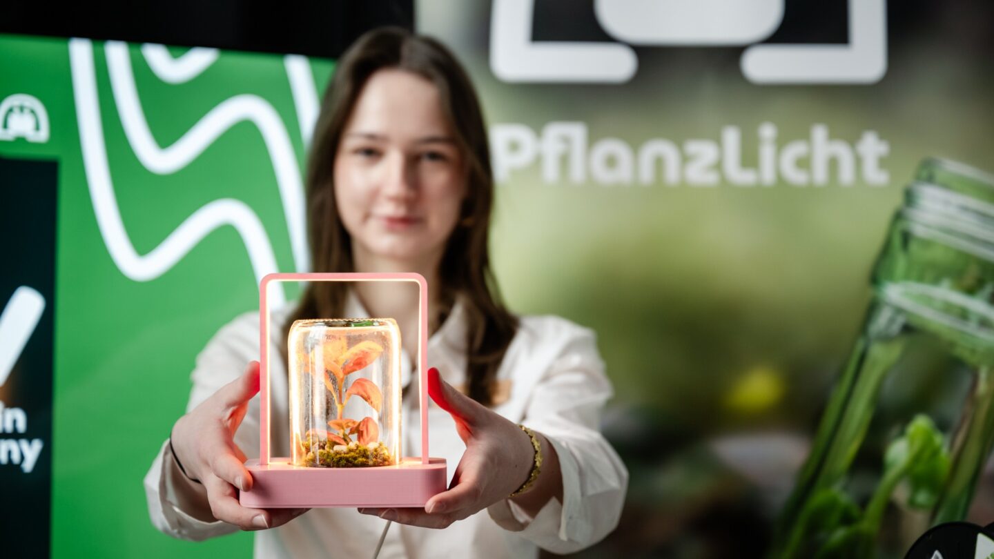 Ein Mädchen hält ein Pflanzenbiotop in den Händen,